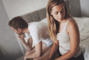 Image is of a man and woman facing away from one another while sitting on their bed, concept of signs of infidelity and what to do in Seattle