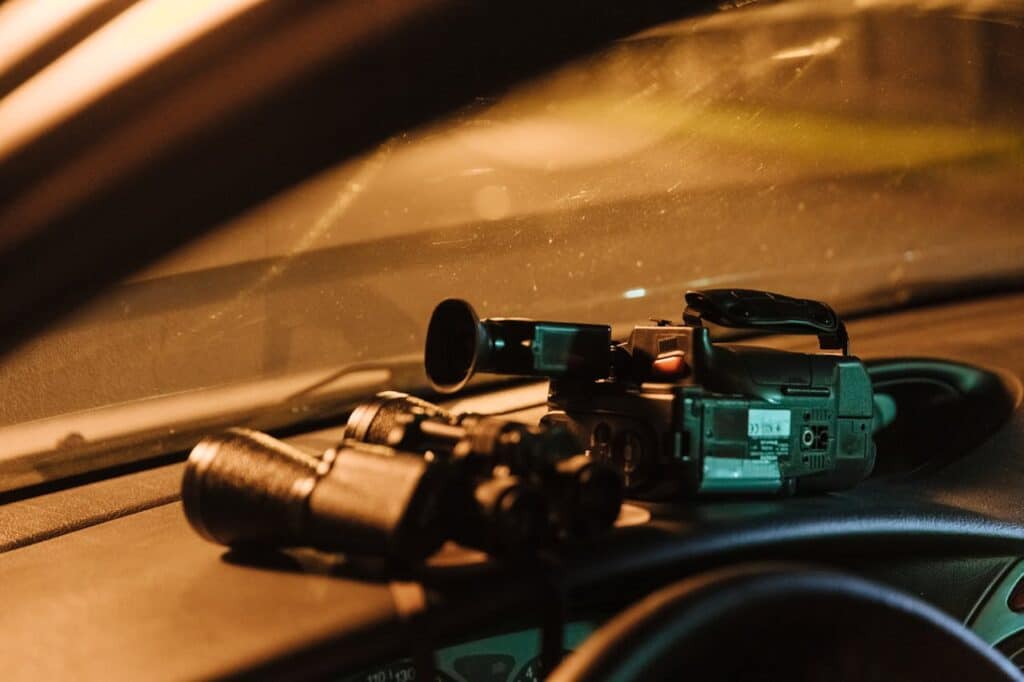 Surveillance tools including binoculars and a camera on a car dashboard.