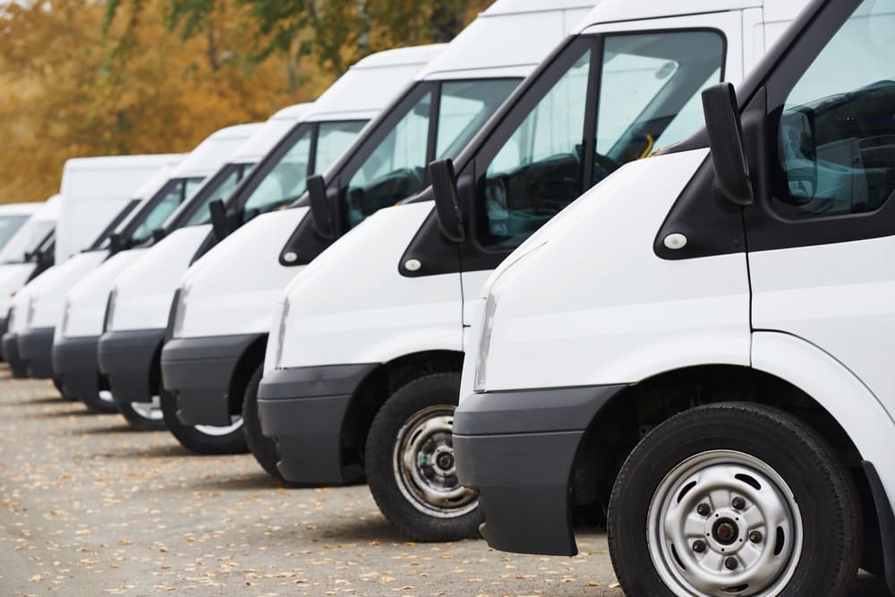 Image is of a long row of white vans lined up outdoors, illustrating how PIs locate hidden vehicles within business fleets or undisclosed company assets.