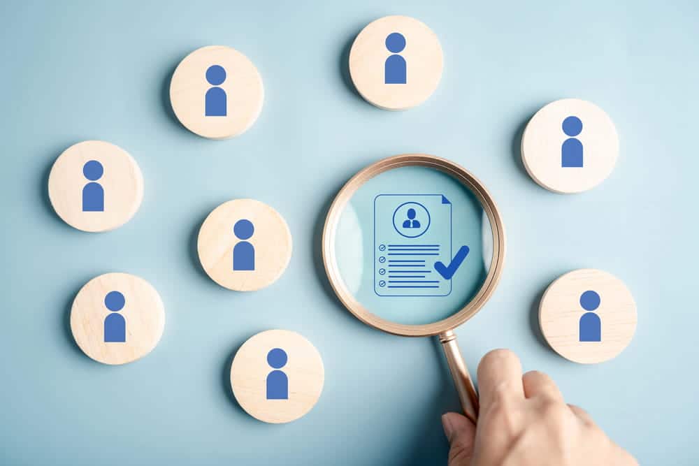 Image is of a magnifying glass examining applicant profiles and a checklist document, illustrating volunteer screening rules used during background review.