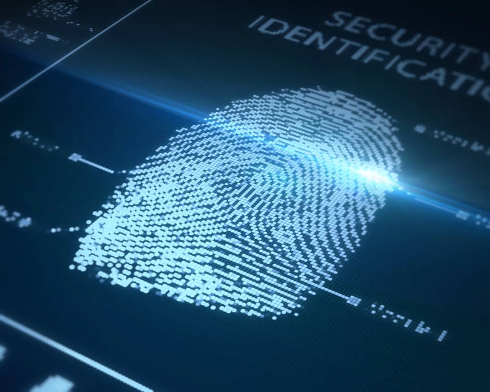 Image is of a person pressing a finger onto a digital scanner, representing fingerprint checks used during background screening and verification procedures.