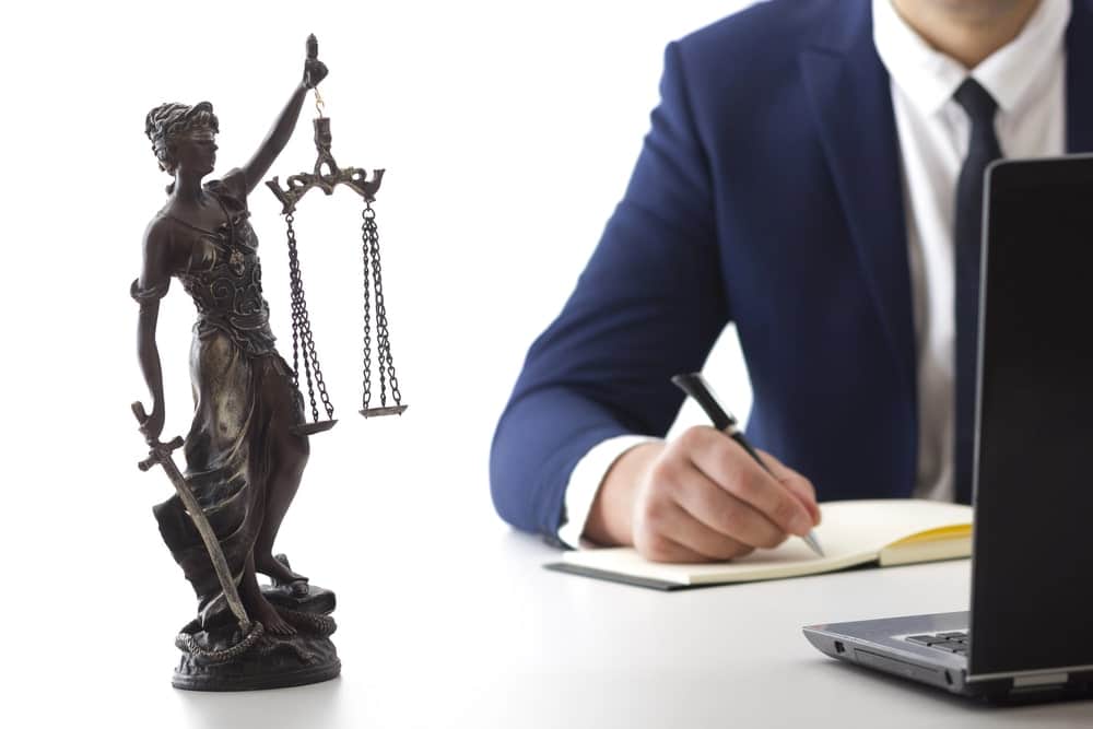 Image is of a lawyer reviewing documents beside a Lady Justice statue, concept of asset search guiding attorneys in enforcement strategy and judgment collection.