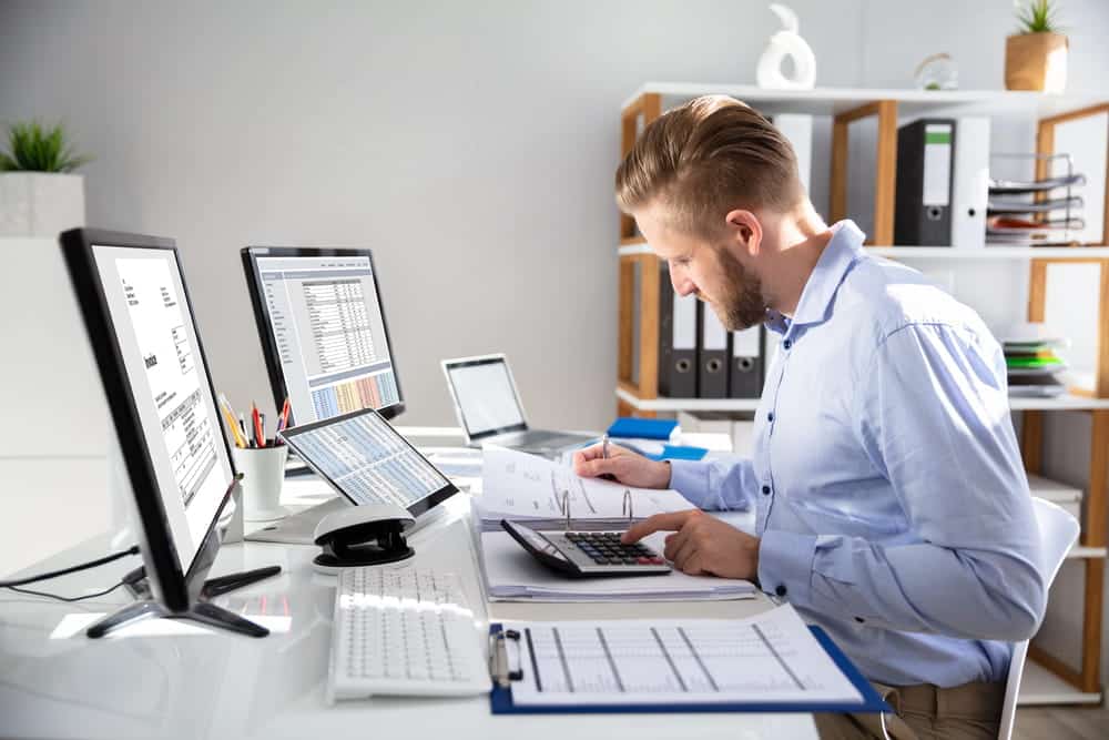 Image is of an accountant reviewing financial records and spreadsheets at a desk, highlighting asset searches used to detect corporate fraud