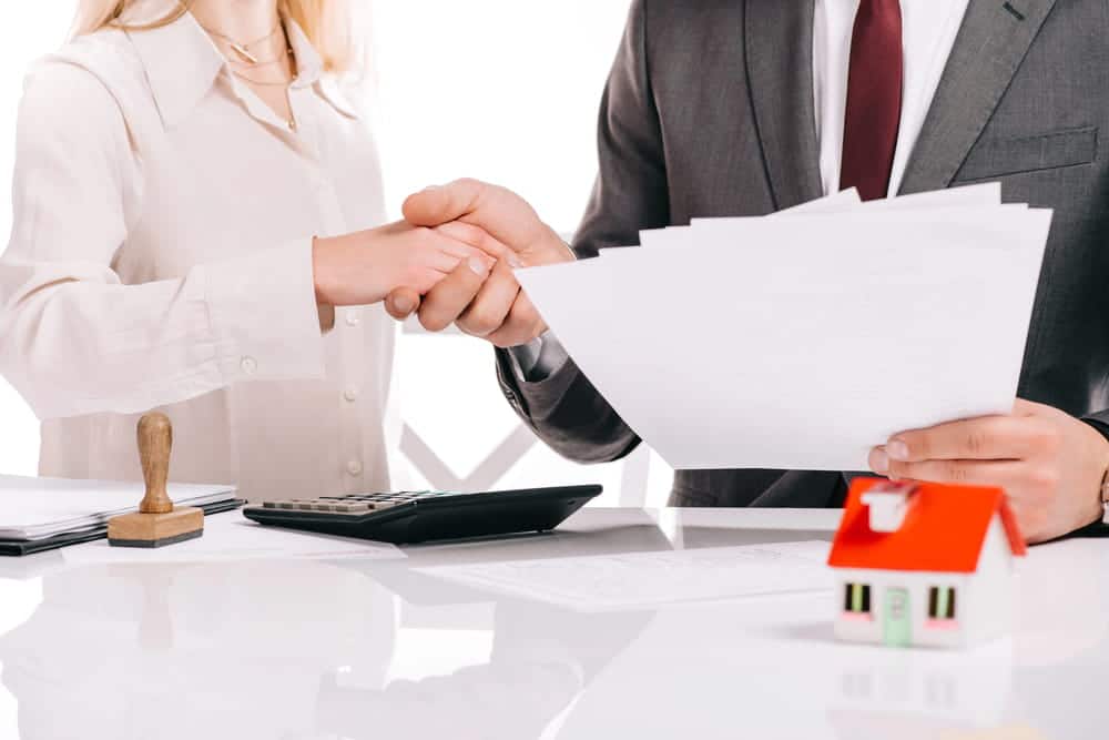 Image is of two professionals reviewing property documents and shaking hands, concept of asset searches used to identify estate property during probate disputes.