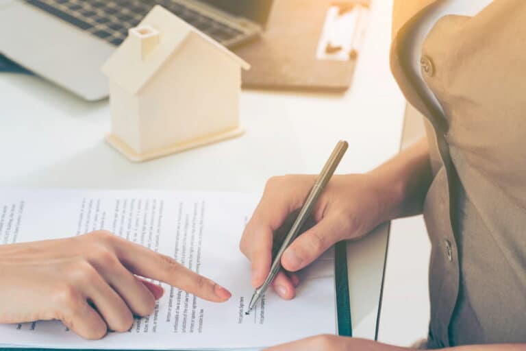 Image is of a person signing a legal document while another points to the paperwork, concept of asset searches used to review financial and property records in probate disputes.