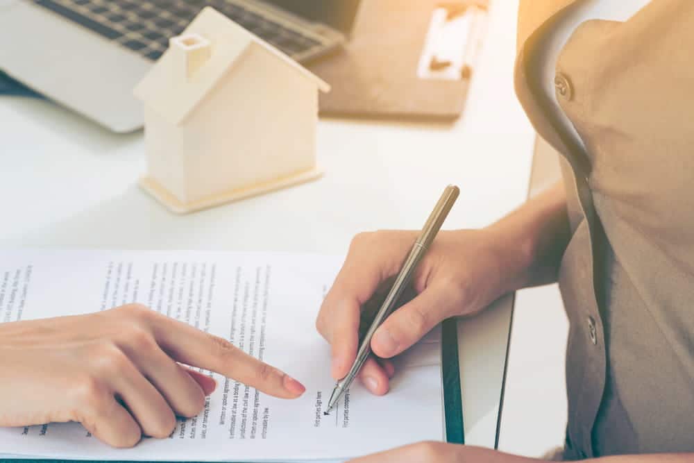 Image is of a person signing a legal document while another points to the paperwork, concept of asset searches used to review financial and property records in probate disputes.