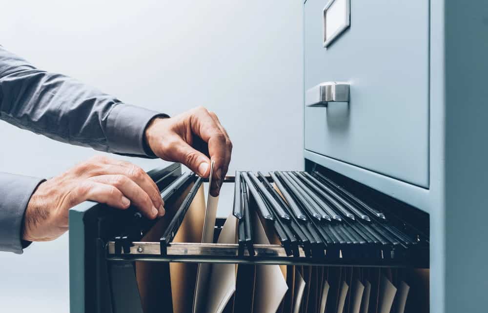 Image is of a person searching through file folders in a cabinet, concept of WA background checks and how records are stored and reviewed